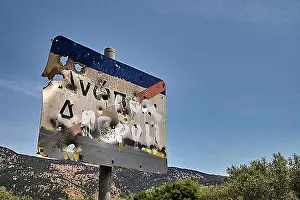 Secure Prints: Weathered road sign with bullet holes against a blue sky and trees in the background