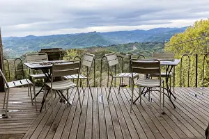 Balcony Prints: White metal tables and chairs sit on a wooden deck overlooking a beautiful valley in the italian countryside