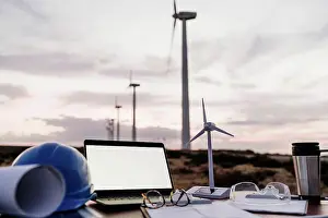 Sustainable Energy Prints: Wind turbine model by laptop with blank screen on desk at wind farm