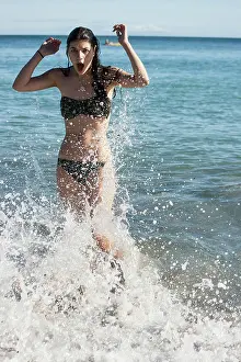 Bikini Prints: Woman in a bikini enjoys the ocean waves splashing around her on a sunny day