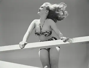 Bikini Prints: Woman in bikini leaning over railing of deck with hair blowing in wind