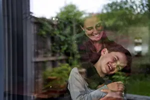Home Prints: Woman embracing cheerful son at home seen through window