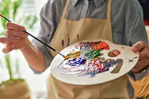 Skilled Prints: Woman holding palette while mixing colors through paintbrush at home
