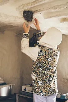 Hood Prints: Woman in hoodie, hands up to swallow's nest under ceiling of old hut