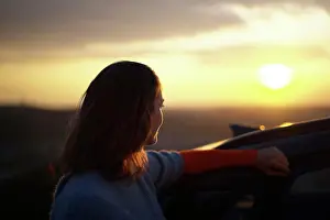 Calmness Prints: Woman leaning on a car watching the sunset