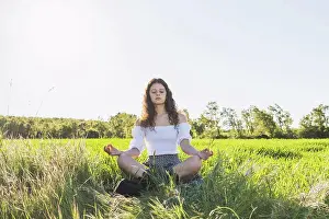 Attractive Prints: woman meditating in the middle of a green wheat field against the sun
