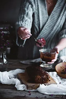 Icing Prints: A woman pouring chocolate icing over a cake in a country kitchen
