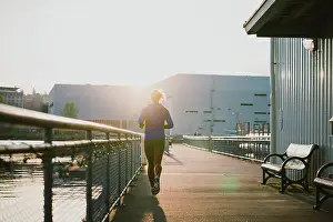 : Woman runs into golden light in early morning on urban paved path