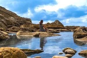 Overlooking Prints: Woman sitting on a rock formation in a coastal landscape