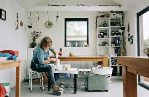 Baby Boomer Prints: woman spinning clay on a pottery wheel in her home studio office in UK
