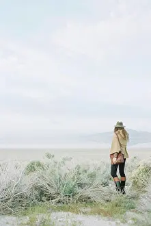 Curiosity Prints: Woman standing in open ground, wearing a hat and carrying a leather bag