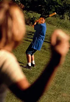 Athletics Prints: Woman throws a baseball to a young man waiting to hit the ball with a bat