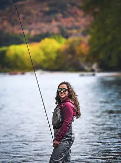 People In Nature Prints: Woman in waders standing in river with fall foliage behind