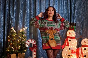 Sweater Prints: Woman wearing festive reindeer ugly Christmas sweater poses with holiday decorations and illuminated snowmen