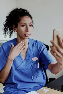 Communications Prints: Worried nurse explaining on video conference while sitting in hospital