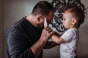1 2 Years Old Prints: One year old boy taking father's temperature at home during isolation