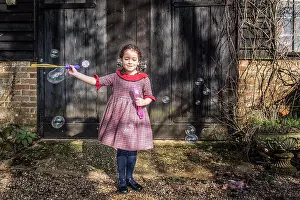 Life Styles Prints: A six year old girl blowing bubbles by a garage door