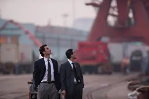 Tours Prints: Young adult businessman and a mid-adult male colleague walking along a shipping yard