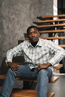 Successful Prints: Young african man sitting on a wooden ladder in a room, portrait