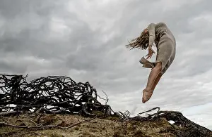 Heaven Prints: From below young ballerina in black wear with upped hands in air near dry branches and blue sky in clouds