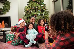 Small Group Of People Prints: Young Black family taking pictures on mobile phone under Christmas tree