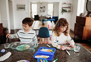 Focused Prints: Young brother and sister coloring with markers at kitchen counter