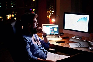 Business And Occupation Prints: Young businessman staring at computer on office desk at night