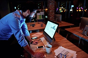 Business And Occupation Prints: Young businessman working at computer on office desk at night