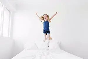 Blond Hair Prints: A young child, a six year old girl in mid air, jumping up and down on a bed