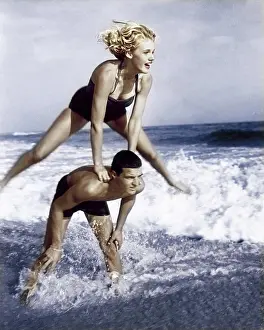 Medium Length Hair Prints: Young couple playing leapfrog in surf