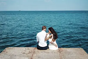 Schoen Prints: Young couple are sitting on the pier by the sea The guy and the girl are sitting on the pier by the sea