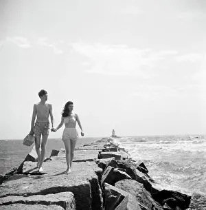 Holding Hands Prints: Young couple walking along groyne
