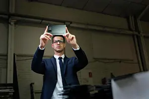 Examination Prints: Young elegant man in suit and glasses using tablet to take photo of workshop conditions in factory