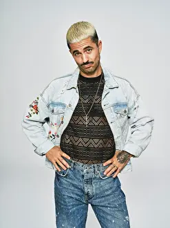 Expressive Prints: Young ethnic man making grimace face looking at camera wearing trendy denim jacket with floral pattern while standing