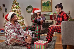 Multiracial Group Prints: Young family and their daughter opening gifts and celebrating Christmas while in their Pajamas