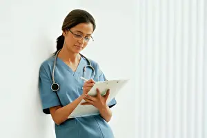 Gown Prints: Young female surgeon writing notes while leaning on wall