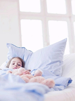 Level Prints: A young girl with brown hair lying in bed holding on to a teddy bear looking at viewer