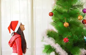 Festive Prints: Young girl looking at a Christmas tree at home. (Children)