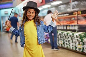 Butcher Prints: Young girl making big gesture with magicians top hat and wand standing in isle of busy grocery store