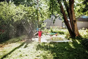 Playful Prints: Young girl runs through sprinkler in backyard during summer