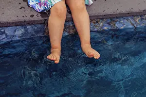 Refreshing Prints: young girl sits by swimming pool, dipping her feet into the water