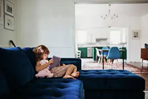 Laying Prints: Young girl sitting on couch in modern living room learning on tablet