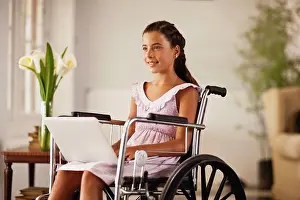 Handicapped Prints: Young girl sitting in a wheelchair looks up from a laptop on her lap and smiles