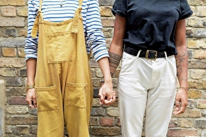 Lesbians Prints: Young lesbian couple holding hands while standing against brick wall