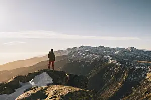 Non Urban Prints: Young man admiring rugged snowcapped mountain landscape at sunset, Gredos, Spain