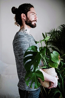 Environment And Nature Protection Prints: Young man looking away while holding Monstera plant at home
