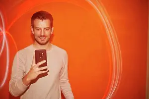 Alicante Prints: Young man looking the smartphone on a orange colored background