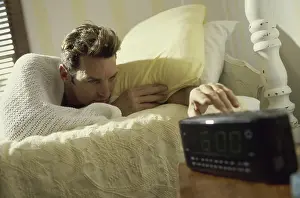 Slow Prints: Young man lying on a bed reaching for the alarm clock