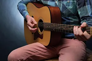 Melodisch Prints: Young man playing on acoustic guitar close up Young man playing on acoustic guitar close up on dark blue background