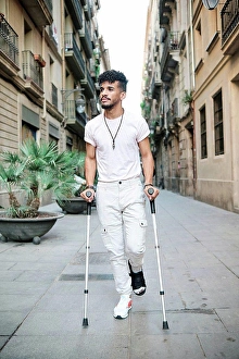 Disability Prints: Young man walking in alley with help of crutches amidst buildings